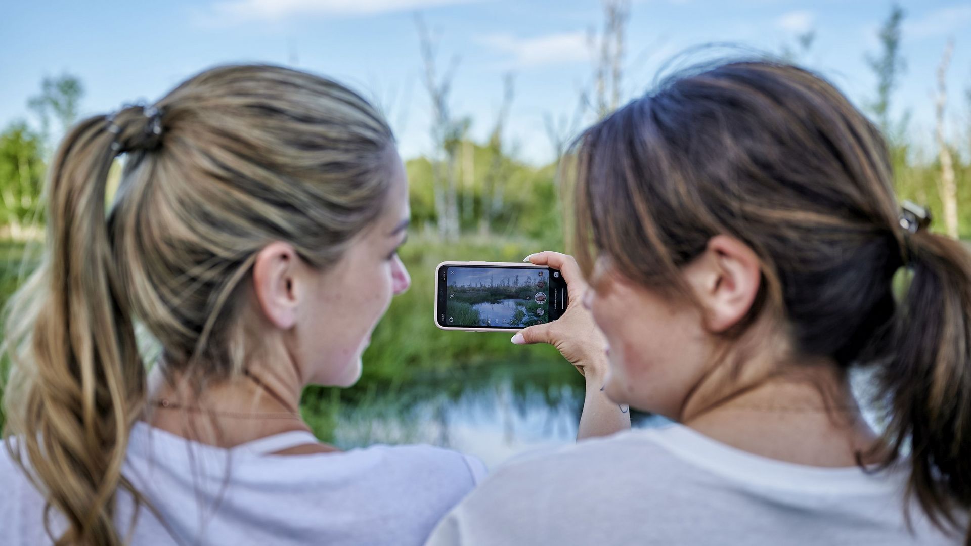 Zwei Frau halten ein Handy vor einem Moorsee hoch