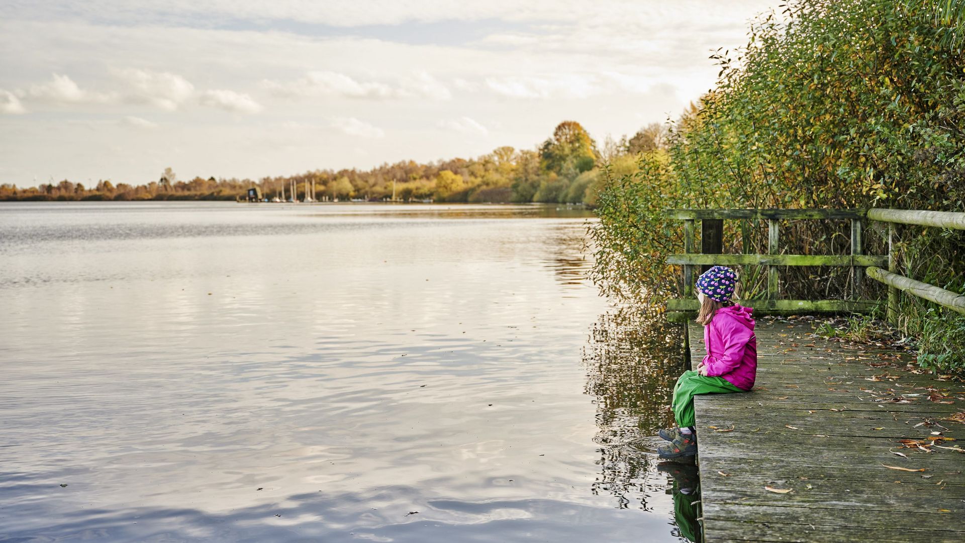 Kind sitzt auf einem Steg und schaut auf das Wasser